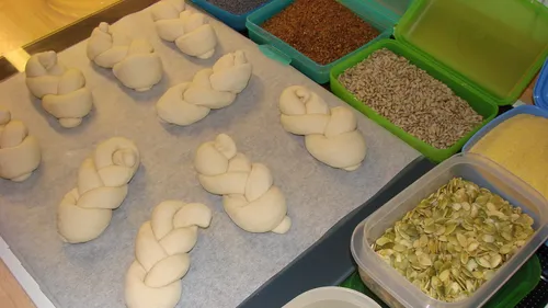 Unbaked bread rolls with seed toppings lined up.