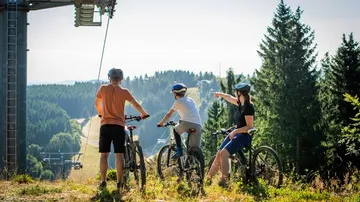 Drei Radfahrer beobachten bewaldete Berglandschaft.