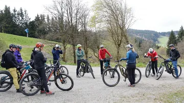 Group of cyclists talking in forest clearing.