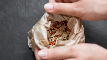 Hands opening paper bag with dried vegetables.