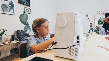 Kind näht mit Maschine in dekoriertem Raum.