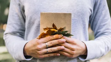 Person holding book with dried leaves outdoors.