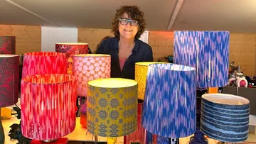 Person smiles behind colorful patterned lamps.