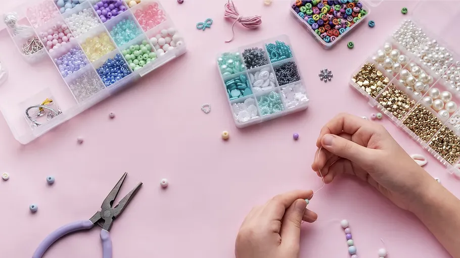 Hands threading beads on pink surface.