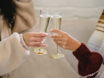 Two people toast on a couch with glasses.