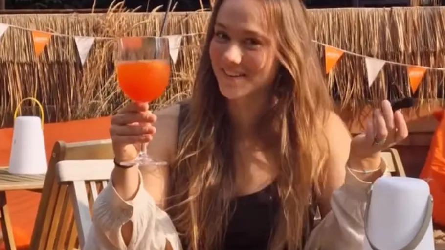 Person holding a drink outdoors, smiling.