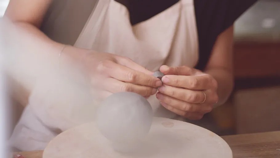 Hands shaping clay at pottery wheel.