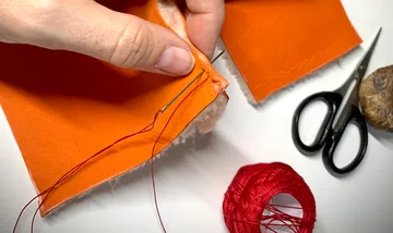 Hand näht orange Stoff mit rotem Faden.