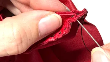 Hands sewing red fabric with needle.