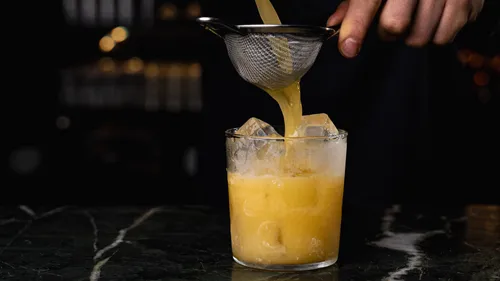 Bartender straining cocktail into glass with ice.