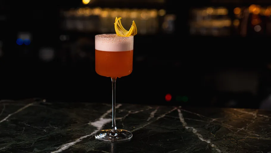 Cocktail with citrus garnish on dark bar.