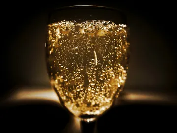 Ein Glas mit sprudelndem, goldenen Getränk in Dunkelheit.