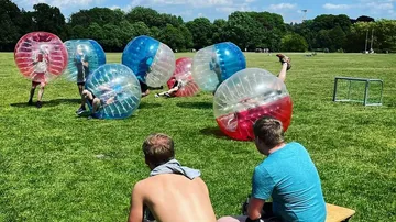 Personen spielen Bubble-Fußball auf Wiese.