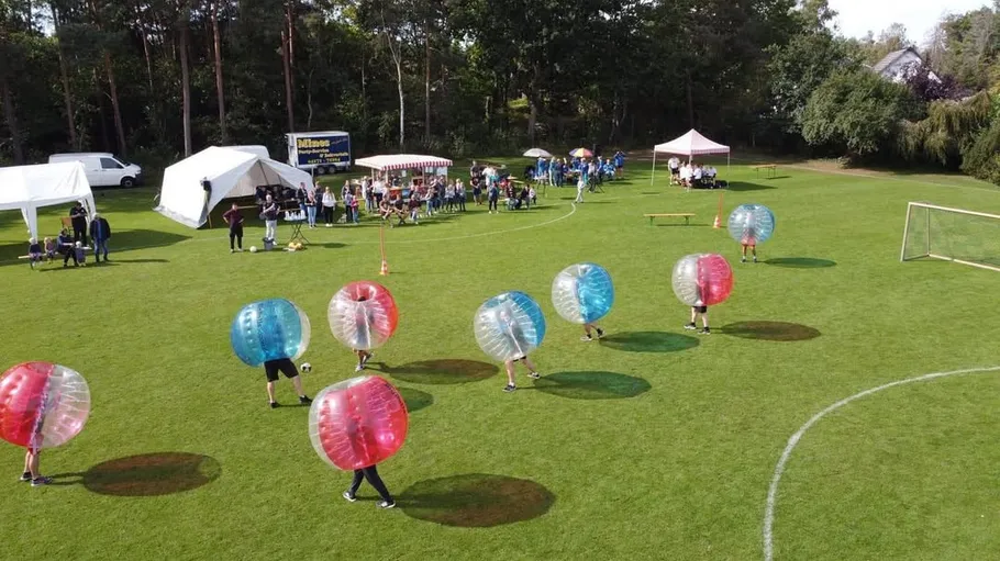 People in bubble balls playing soccer on grass field.