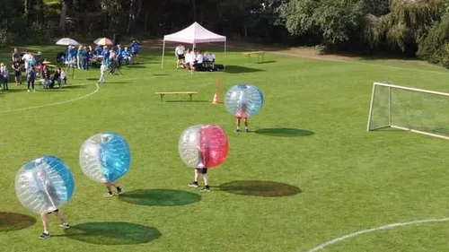 People in bubbles playing soccer on grass.