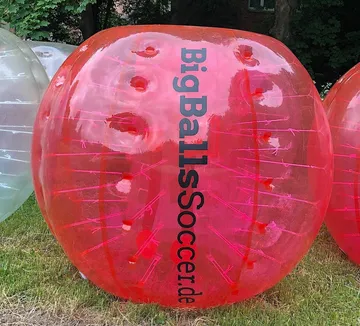 Roter aufblasbarer Ball auf Rasen mit Bäumen.