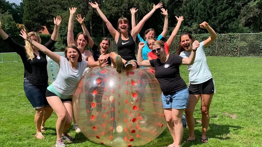 Group celebrating around inflatable ball outdoors.