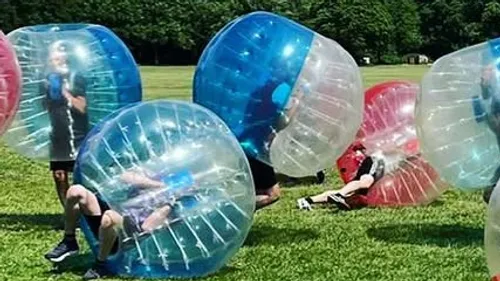 People playing bumper ball on grassy field.
