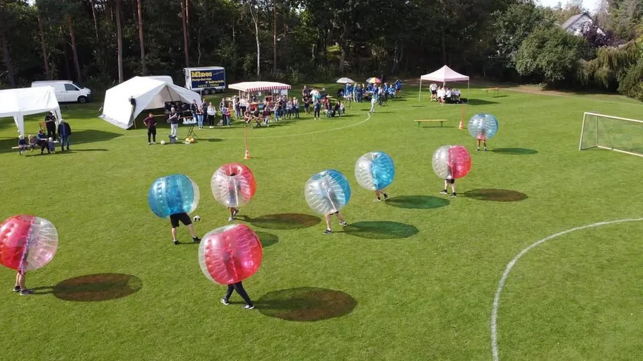 People playing bubble soccer on grassy field.