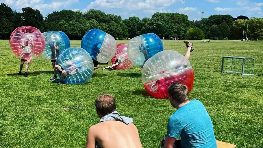 People playing bubble soccer on grassy field.