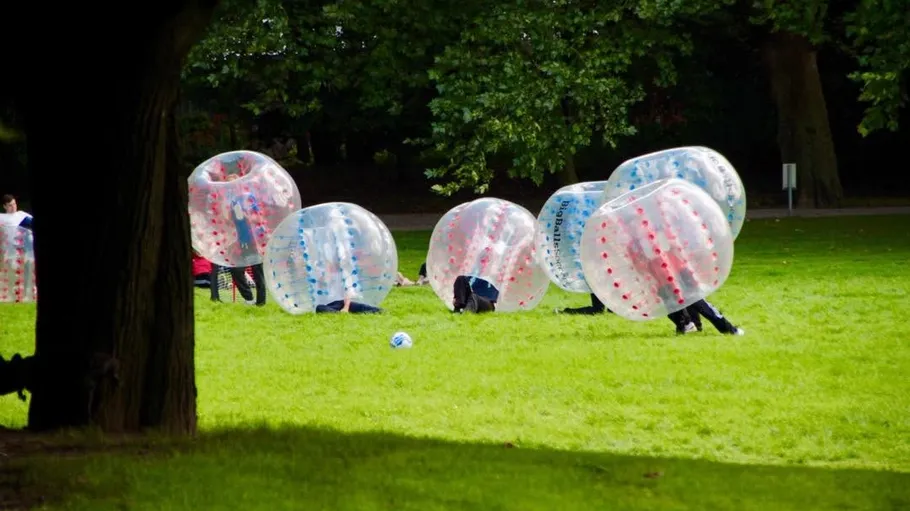 People playing bubble soccer in a park.