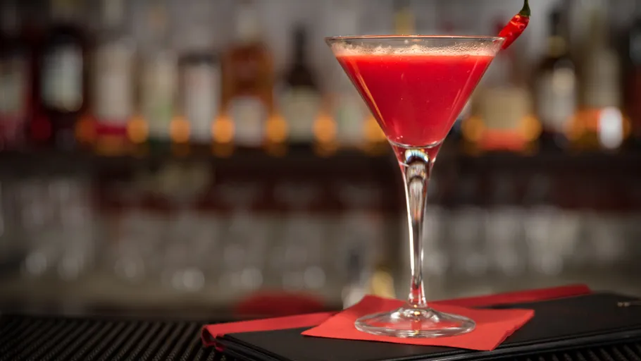 Red cocktail with chili on bar counter.