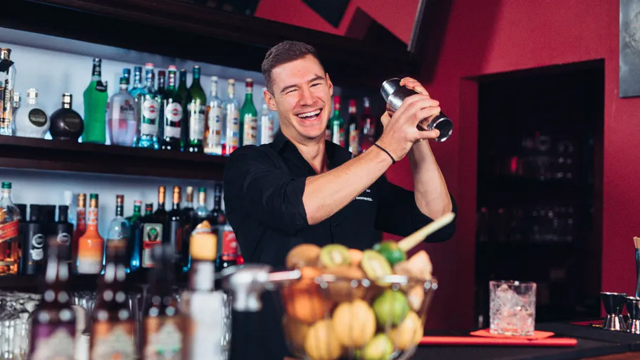 Bartender smiling while shaking cocktail mixer.