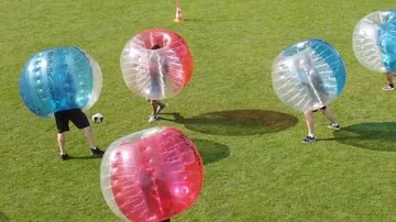 Menschen spielen Bubble-Fußball auf Rasenfeld.