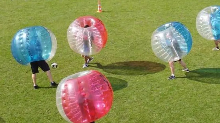 People playing bubble soccer on grass field.
