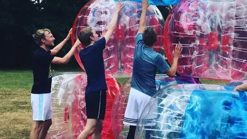 Three people stacking inflatable clear balls outdoors.