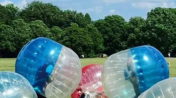 People in inflatable balls on grassy field.