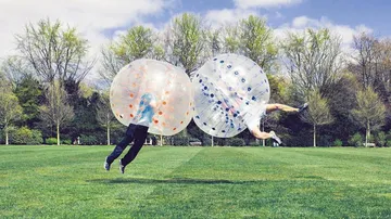 Two people colliding in inflatable balls outdoors.