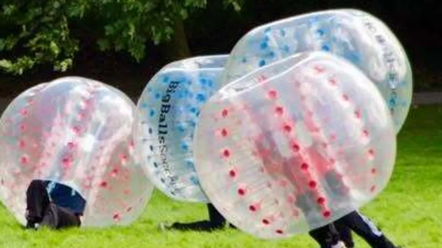 People in inflatable bubbles playing on grass.