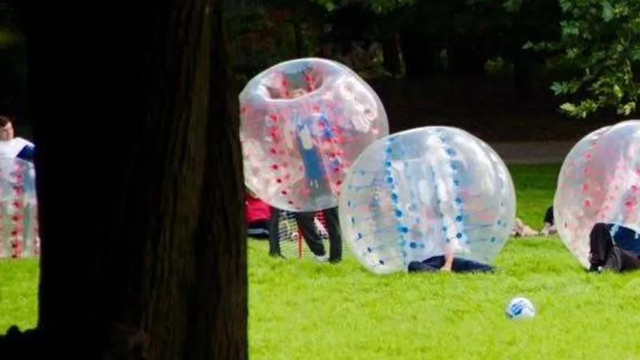 People playing bubble soccer in a park.
