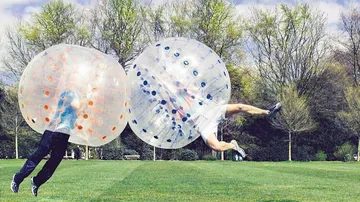 Two people collide in inflatable balls outdoors.