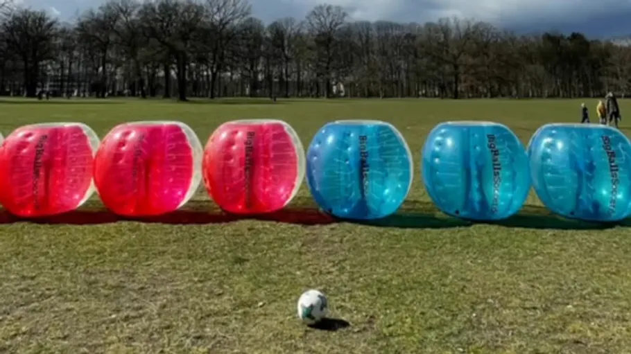 Six bubble soccer balls on grassy field.