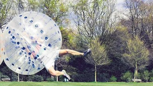 Person inside inflatable ball, jumping in park.