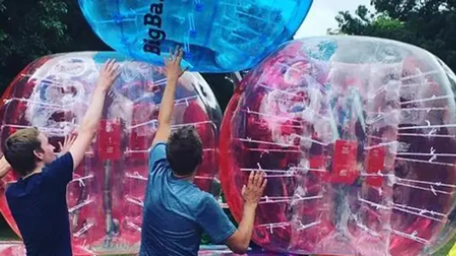 People playing bubble soccer in a park.