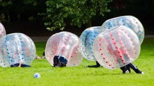 People in inflatable balls playing on grass.