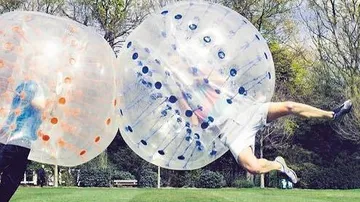 Two people collide inside inflatable balls outdoors.
