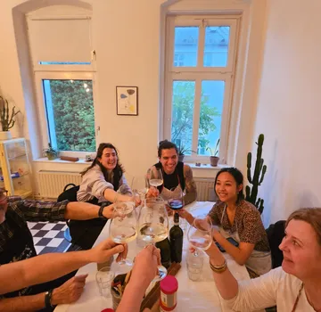 Gruppe stößt am Esstisch in gemütlichem Raum an.