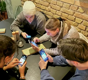 Vier Personen nutzen Smartphones an einem Tisch.