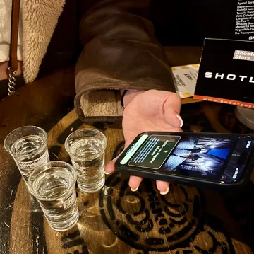 Person holds phone beside three shot glasses.