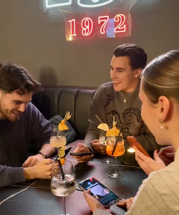 Personen am Telefon, in einer Bar sitzend.