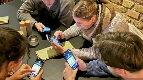 Four people looking at smartphones, sitting at table.