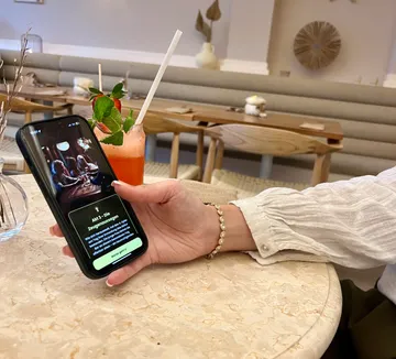 Person holds phone displaying app in cafe.