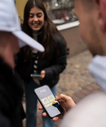 Person using phone outdoors, friends nearby.