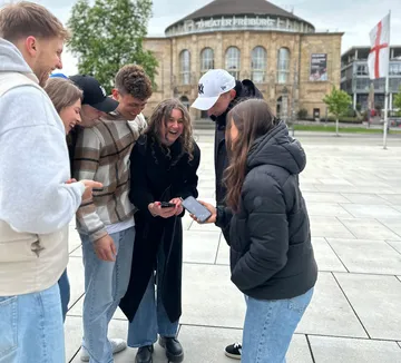 Gruppe von Freunden lacht über Handy draußen.