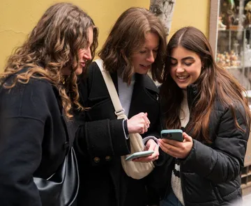 Three women looking at a smartphone outside.