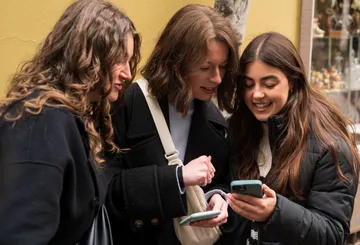 Three women looking at smartphones outside.